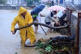 A man in a yellow raincoat lifting a branch out of calf-deep water. 