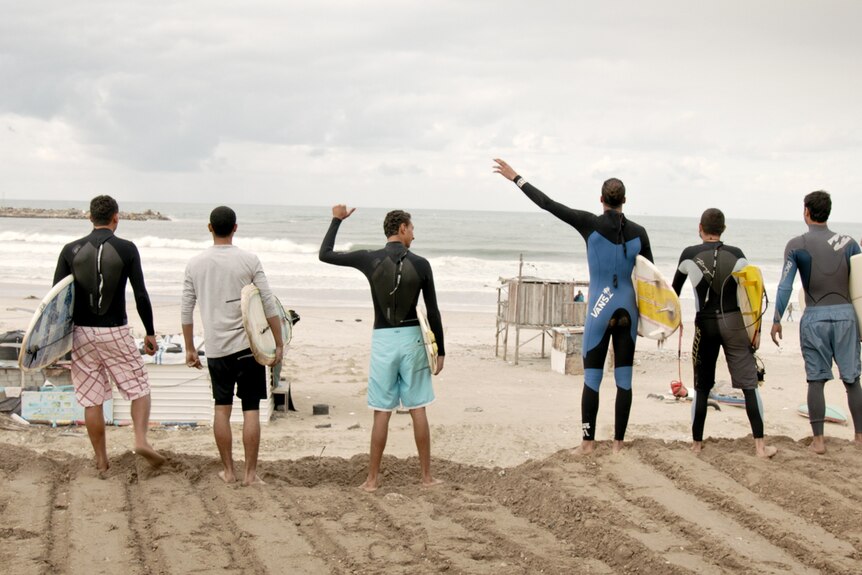 a group of surfers standing on a beach looking to the sea