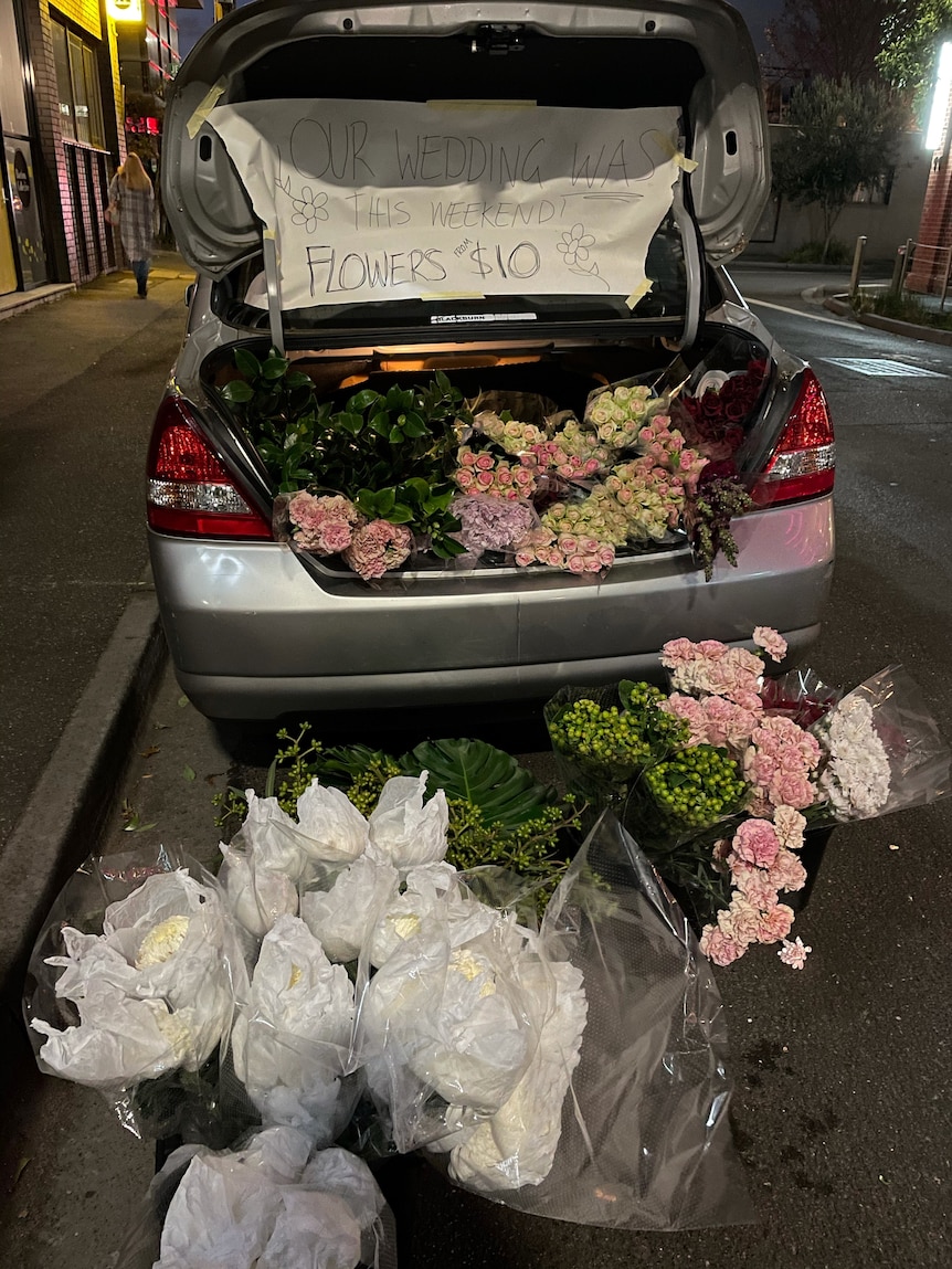 Un coffre de voiture avec des fleurs et un signe de vente écrit sur carton.