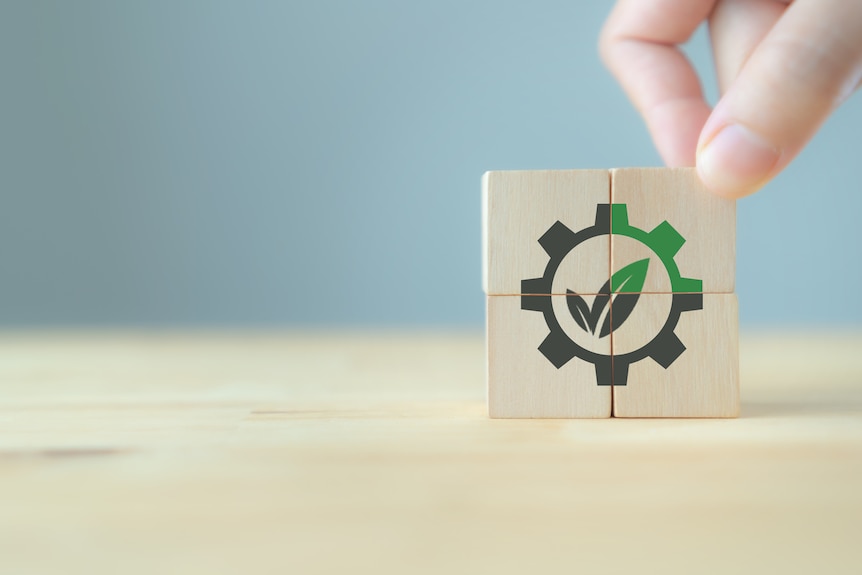 Image of a hand with four puzzle blocks stacked together forming a eco tick. Only one part of the four blocks is green.