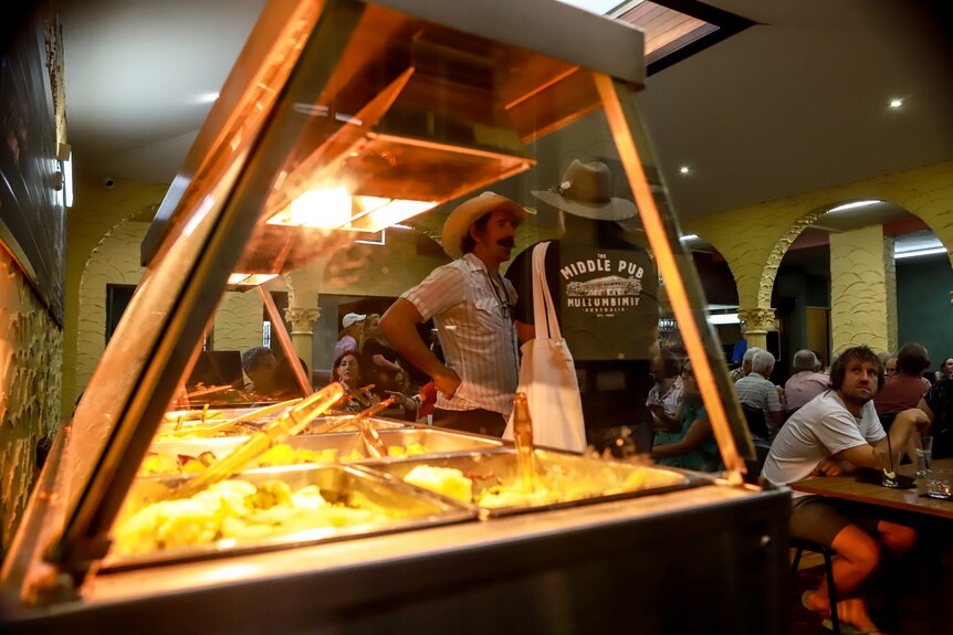 Yellow tinted bain marie with vegetables in foreground, people standing in pub in background