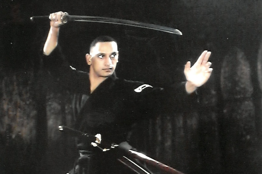 a man in a black robe wields a weapon in a martial arts position