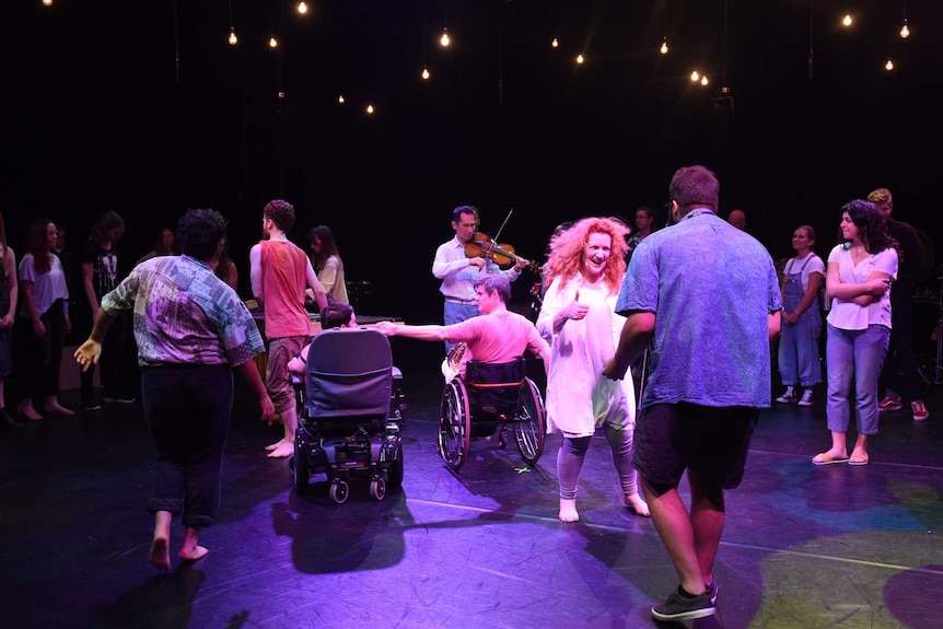 Group of people on stage, including two wheelchair users, someone who appears to be singing.