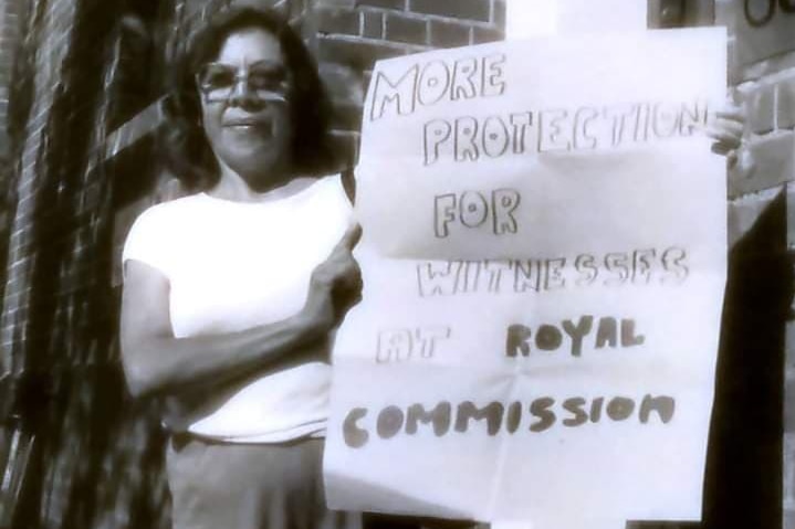A woman holds up a sign that reads: More protection for witnesses at royal comission