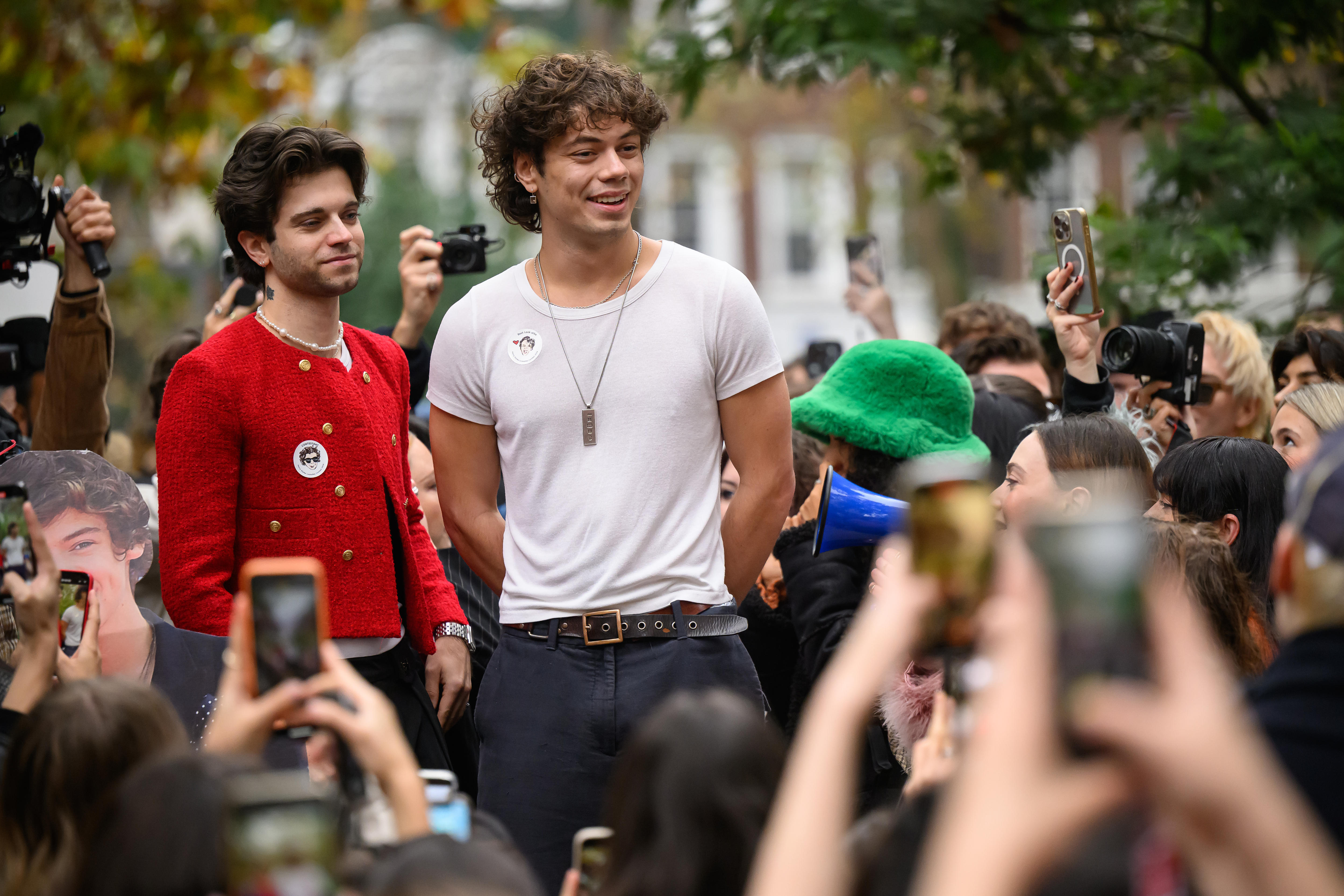 A man in a white tshirt and a man in a red long sleeve jumper standing in front of crowds