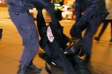 A person yells as they are carried by two police riot gear.