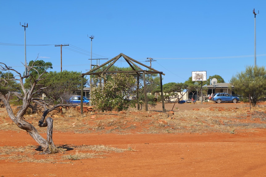 A gazebo with no cover, red dirt and cars 