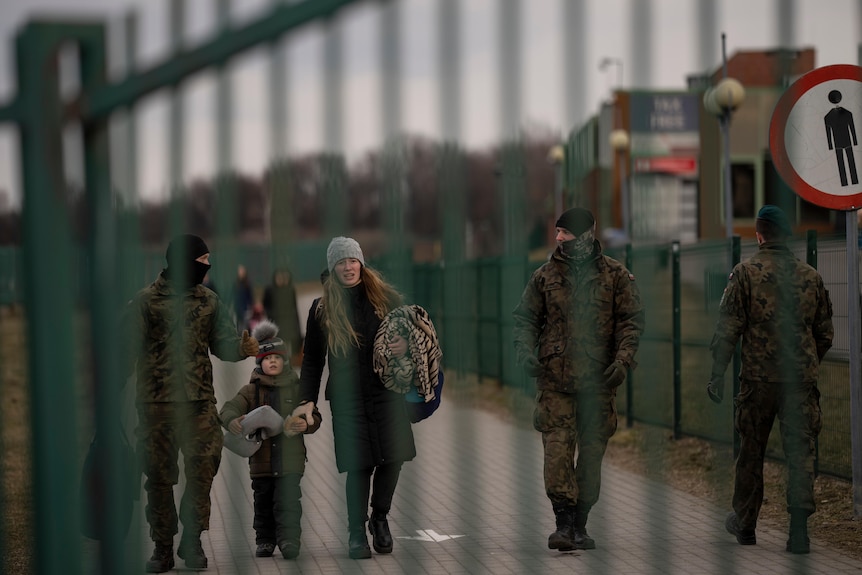 A woman and child walk along a footpath accompanied by soldiers. 