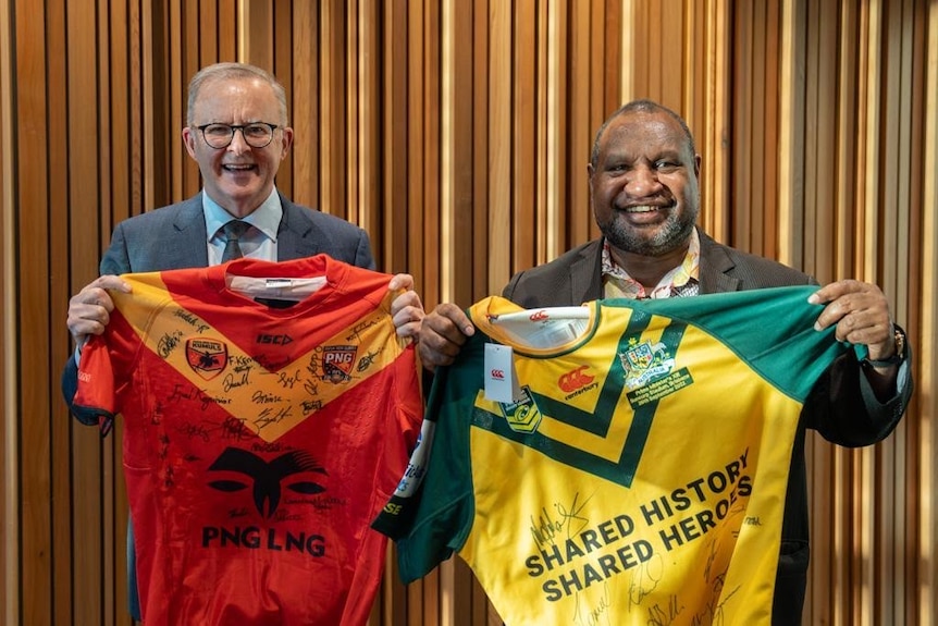 Australian and Papua New Guinea Prime Ministers hold up each countries respective signed  jerseys at the PM XIII 2022 Lang Park 