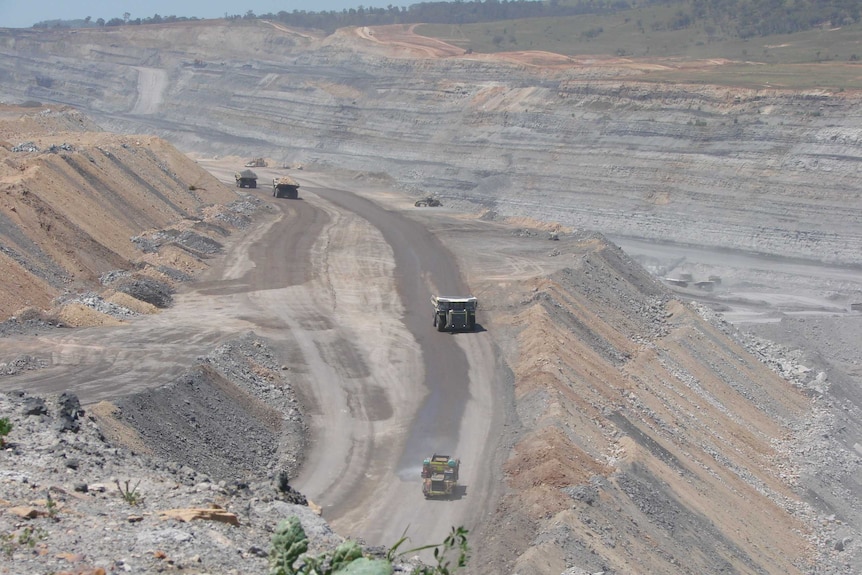 An aerial view of an open-cut mine with huge trucks driving along one of its dusty roads.