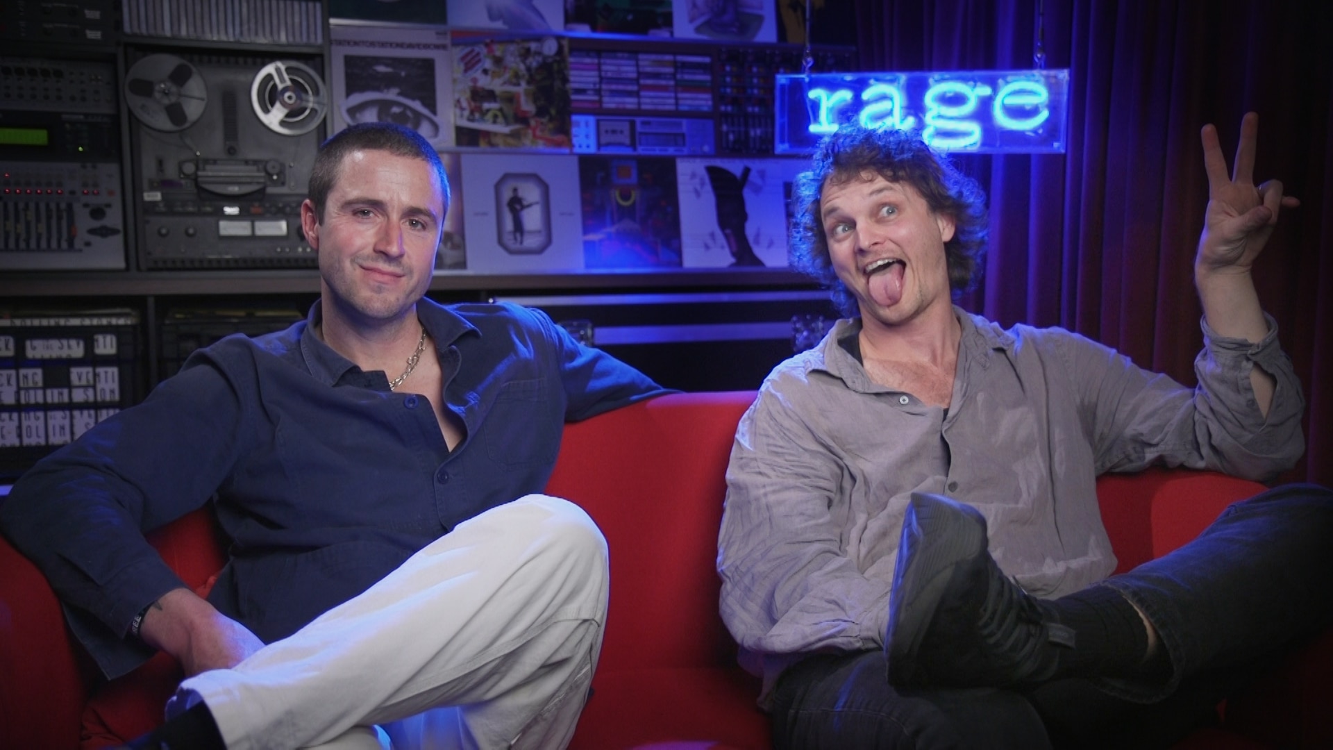 King Gizzard and the Lizard Wizard's Joey and Stu sit on a red couch in front of a neon blue sign that reads rage