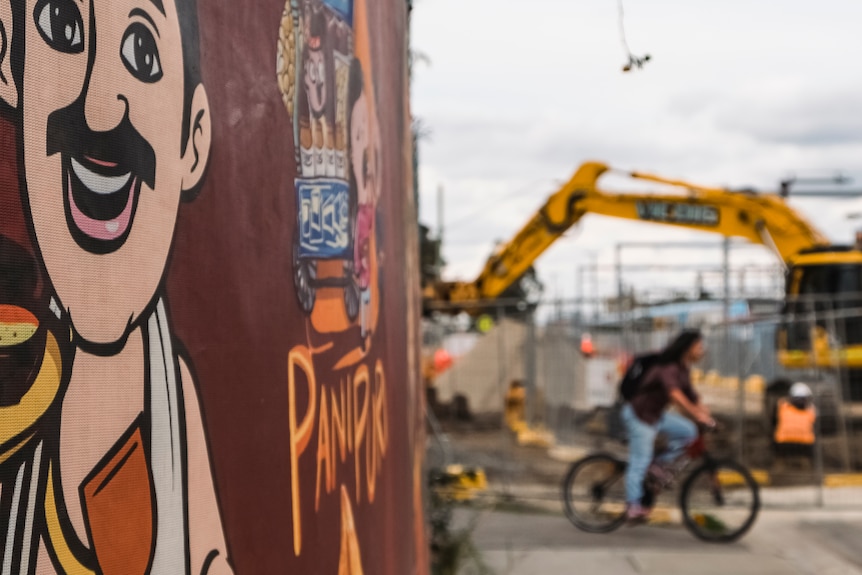 A bicyclist is riding past a construction site. There is a mural in the foreground.
