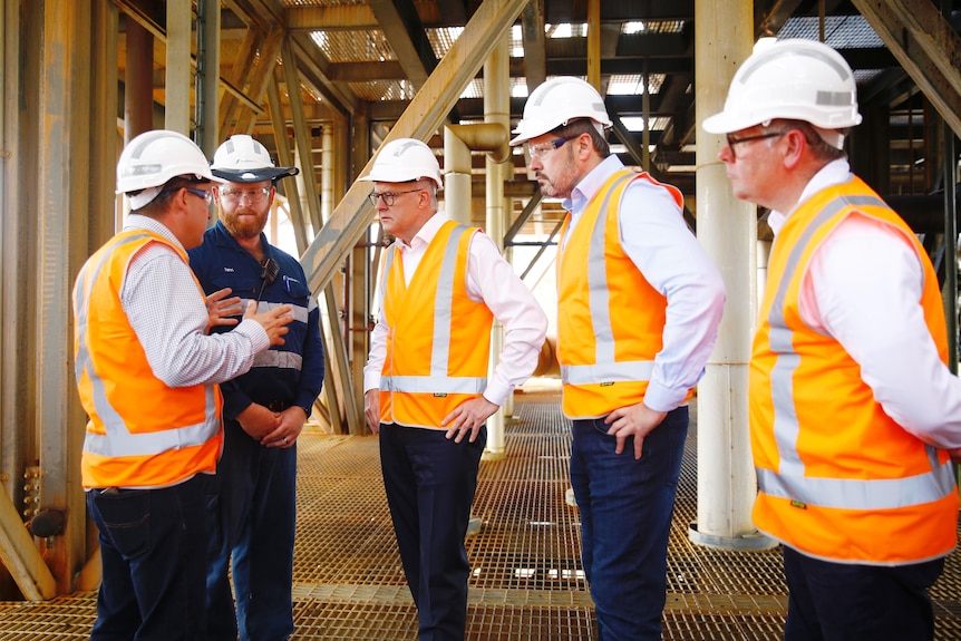 Four men in high-vis listen to another man speak. 