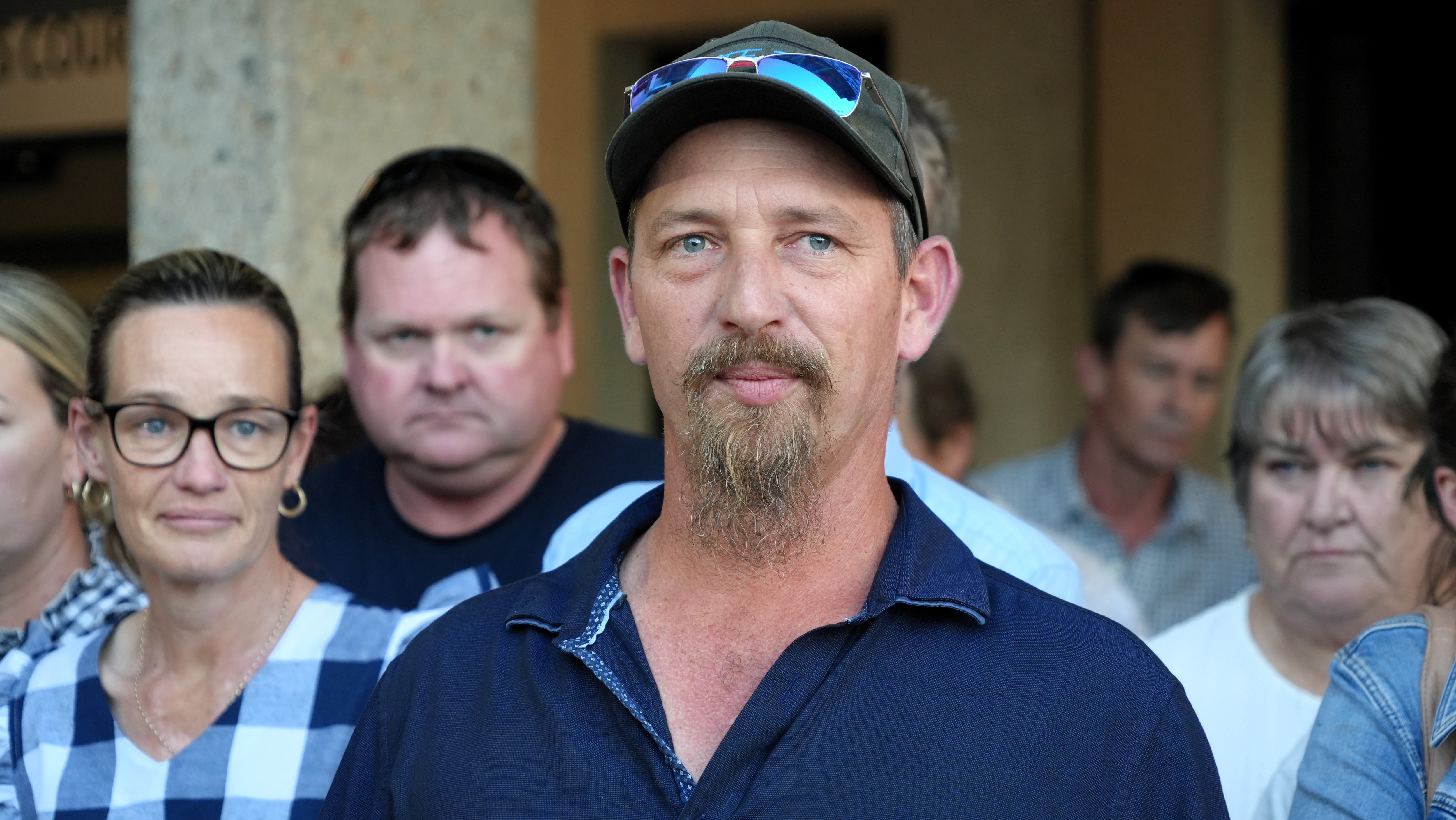 A young man wearing a blue shirt with a goatee and cap. 