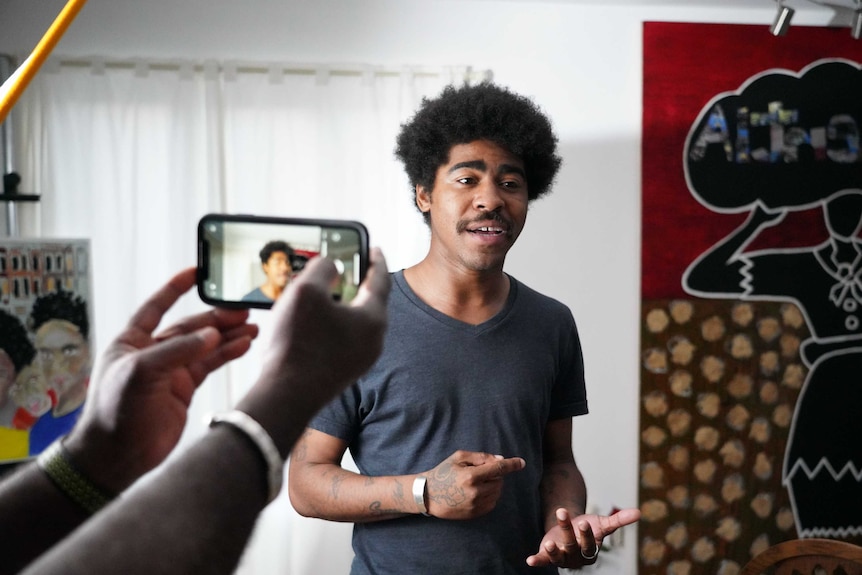 Devin Allen, gestures with his hands while speaking. Another person's hands can also be seen holding out a phone to take a photo