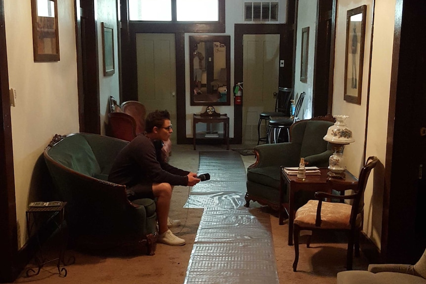 A man sits alone in a hotel room staring at a wall.