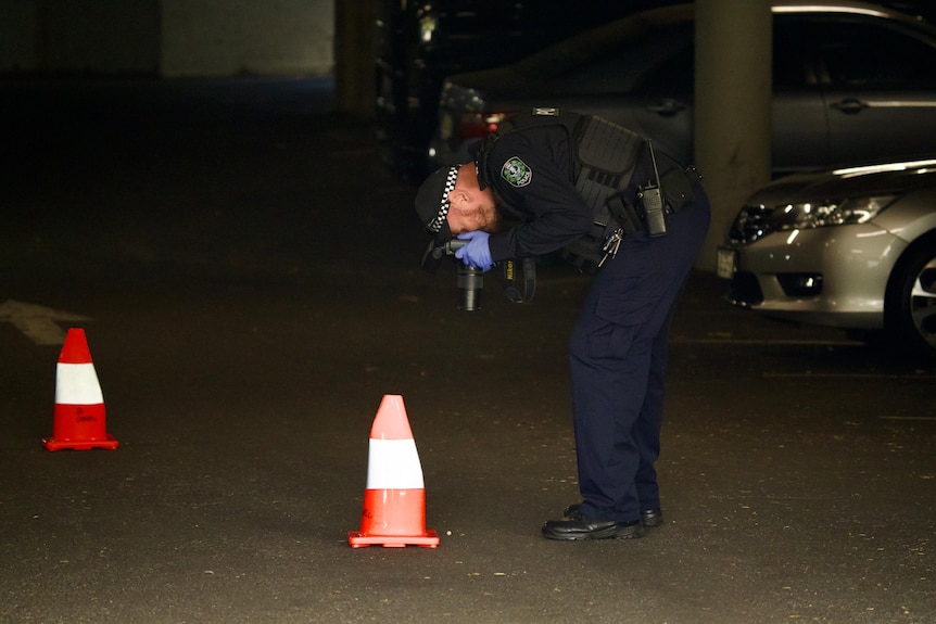 A police officer bends over to take a photo of evidence on the ground in a dark car park