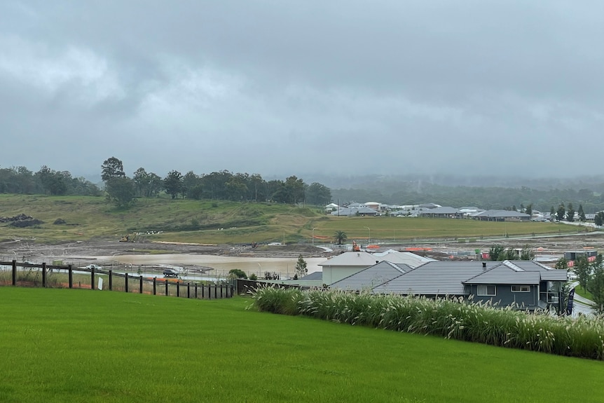 A damn can be seen over a hill next to a housing estate