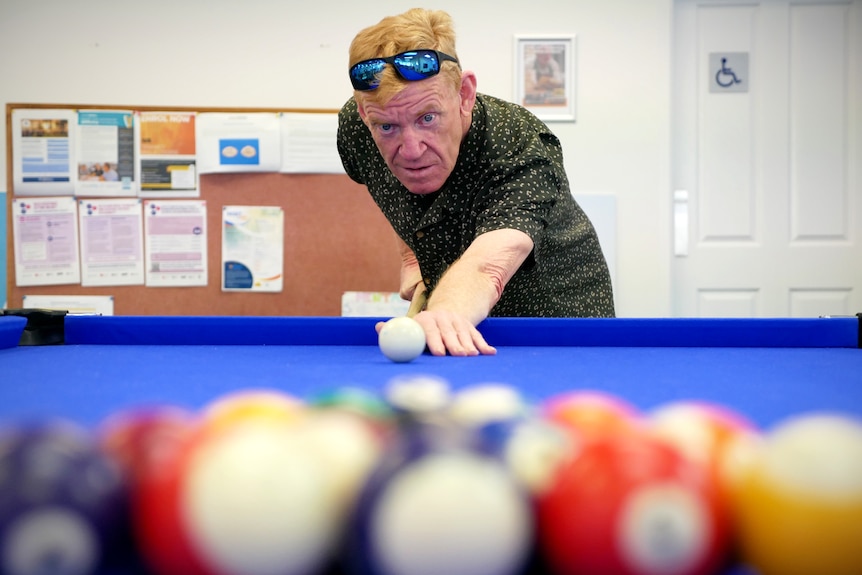 A man leans against a pool table as he prepares to break