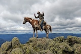 A man waving from a horse on top of a mountain.