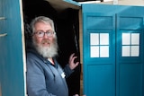 A man stands inside an upright blue coffin designed to look like Dr Who's tardis