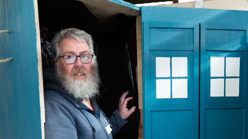 A man stands inside an upright blue coffin designed to look like Dr Who's tardis