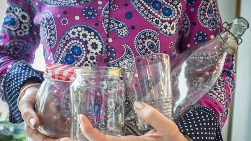 A lady holds glass jars and bottles in her arms.