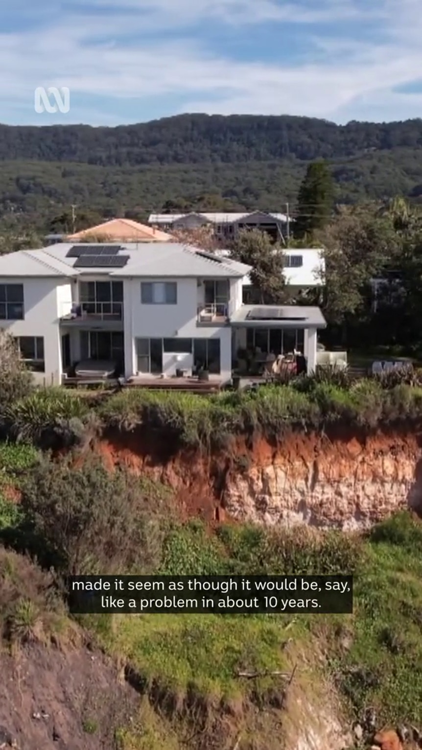 A modern house sits atop a cliff with crumbly looking sides