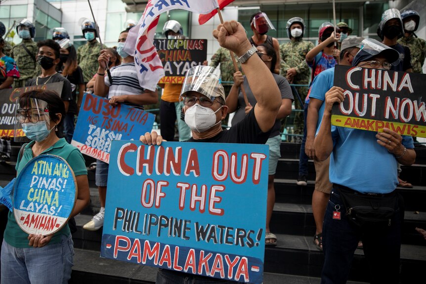 Protestors hold up blue signs saying china out of the philippine waters 