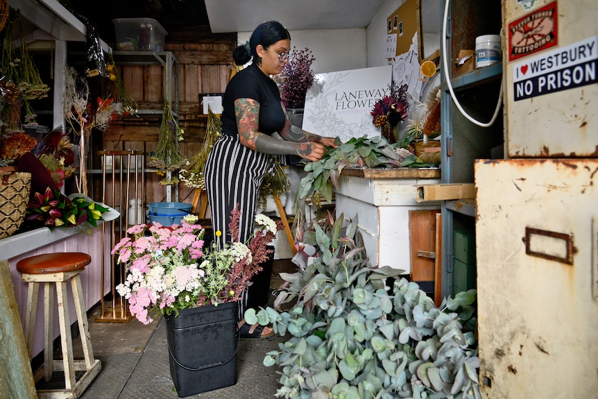 A florist works in a shed full of flowers and foliage. 