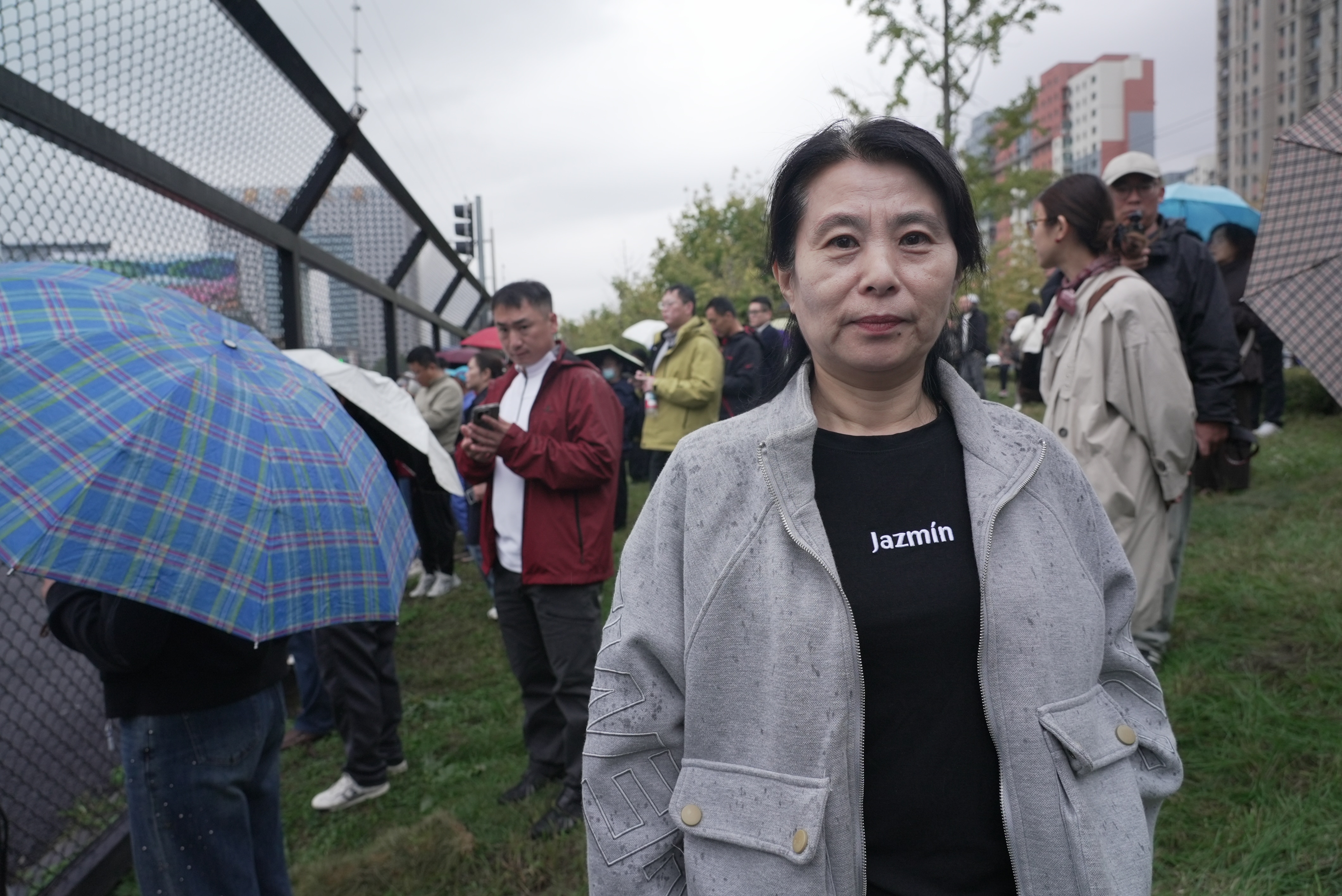 Ms Wu stands beside a tall fence, among a crowd of onlookers