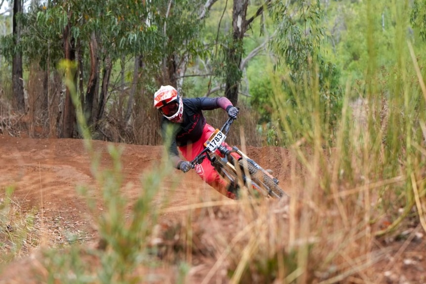 A teenager with a helmet and visor on rides a mountain bike with protective gear on. 