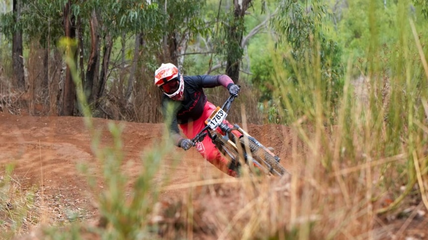 A teenager with a helmet and visor on rides a mountain bike with protective gear on. 
