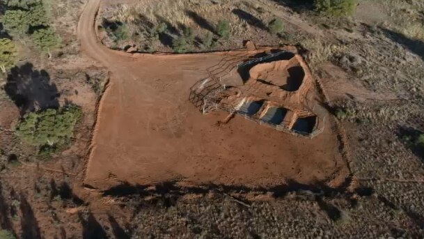 Still from aerial drone footage showing a bore hole in an area of sparse scrub.