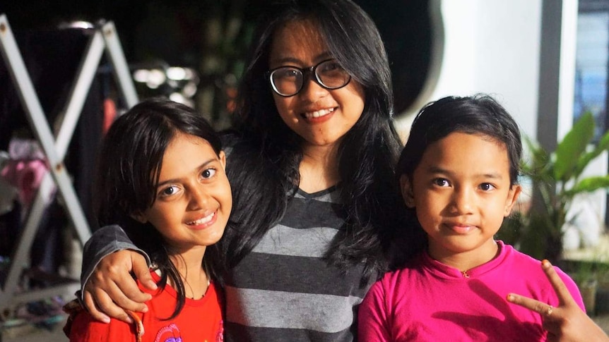A woman wearing glasses and her two younger girls smile for the camera.