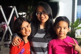 A woman wearing glasses and her two younger girls smile for the camera.