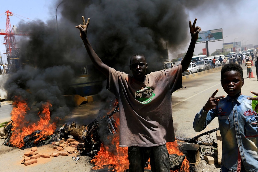Sudanese protesters cheer as they burn tyres and barricade the road.