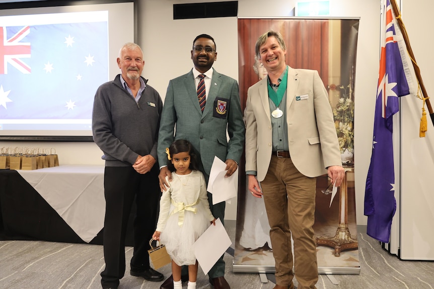 A smiling man and his daughter stand with municipal officials at a citizenship ceremony.