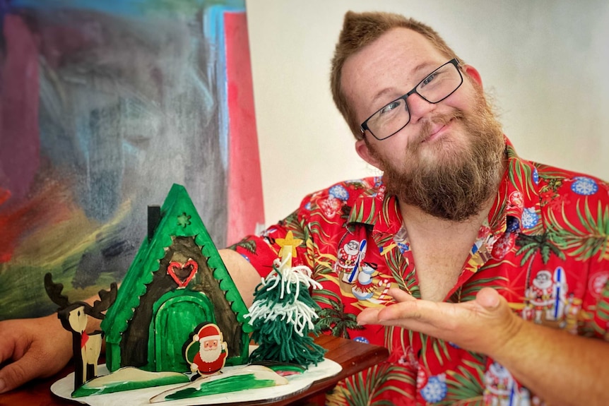 William Grier in a Christmas shirt next to a Christmas tree he built out of craft supplies.