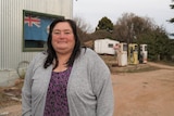 A woman in a grey cardigan standing in front of an old petrol station