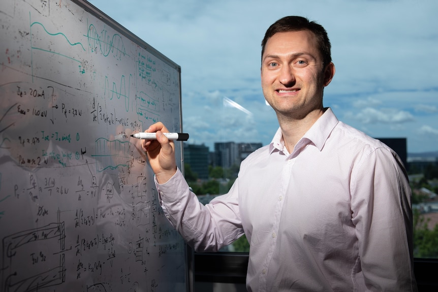 A man stands in front of a whiteboard writing code.