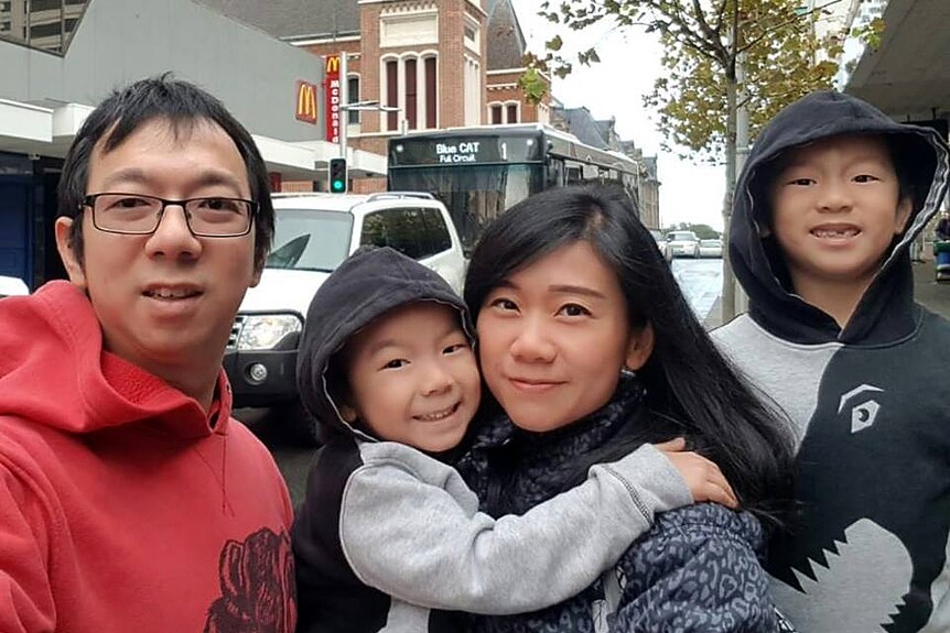 A father, mother and two boys take a selfie in the Perth city with a clock tower in the background.