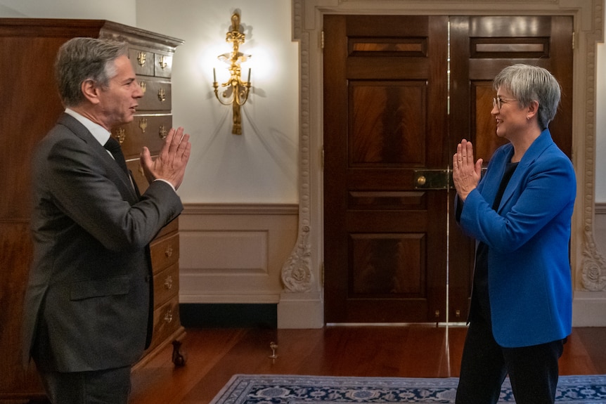 Antony Blinken and Penny Wong bow to each other in a meeting room 