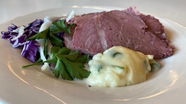 A photo of the cooked corn beef on a plate with white sauce and herbs
