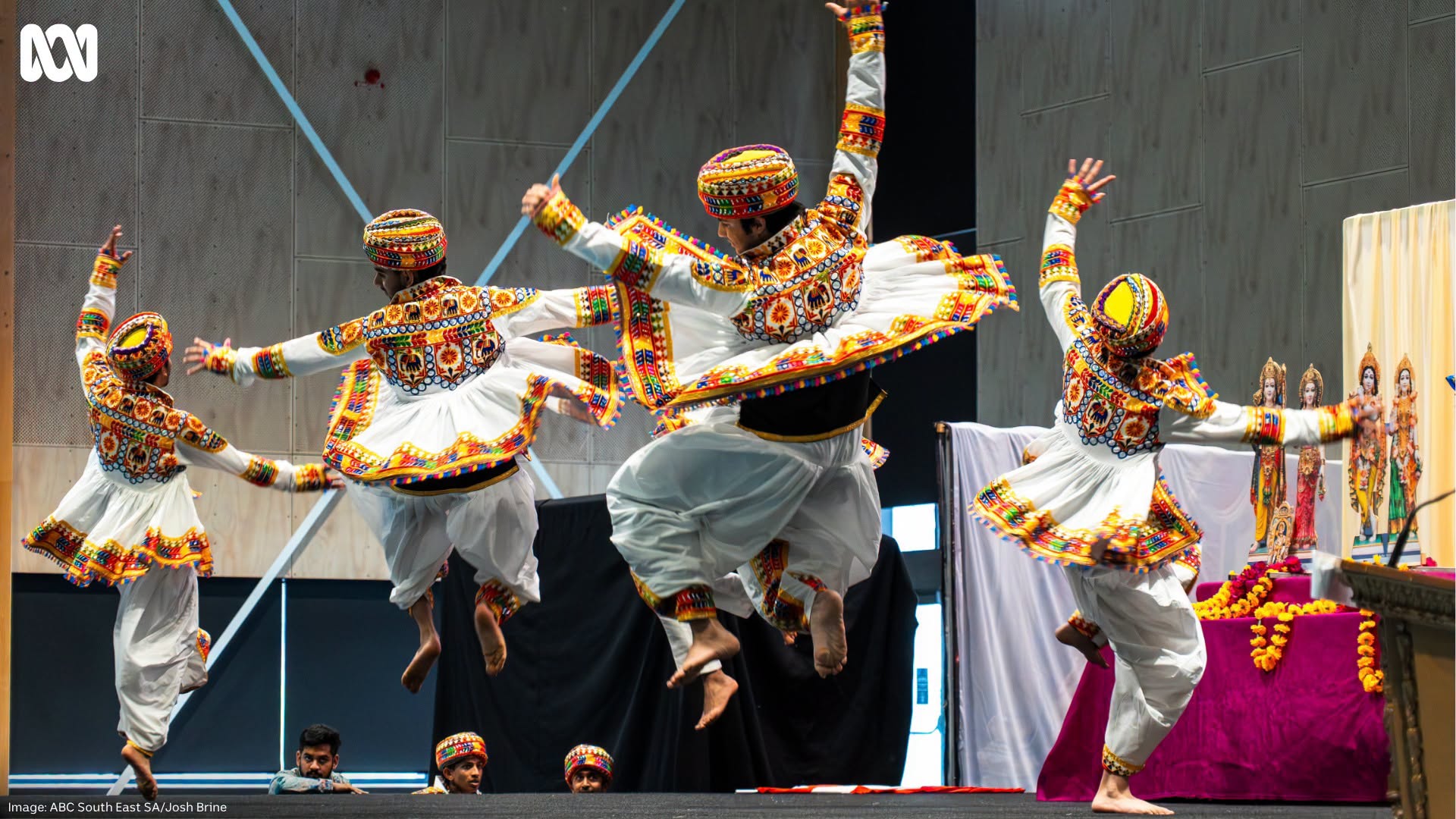 People dressed in colourful Indian costumes dancing high, in red, white and yellow.