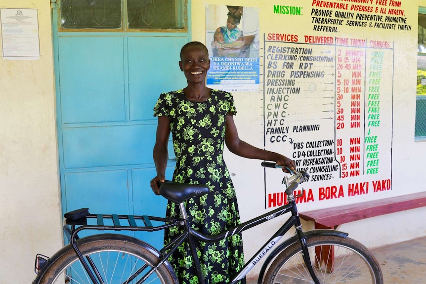 Lady standing with a bike in front of a blue door.