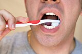 Close up of a man brushing his teeth with a red toothbrush.