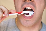 Close up of a man brushing his teeth with a red toothbrush.