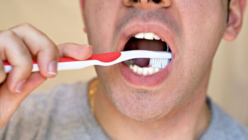 Close up of a man brushing his teeth with a red toothbrush.