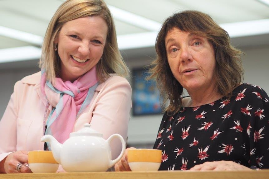 Two women sit down to share a pot of tea.